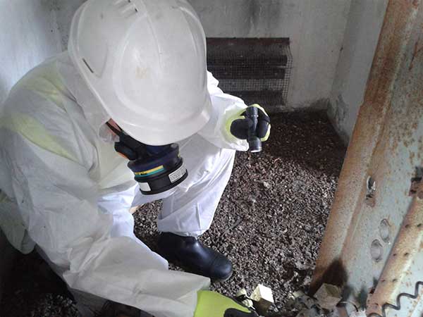 Worker in a protective suit and respirator performing asbestos removal